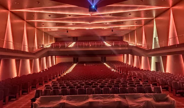 Large auditorium with lit angled side walls and a full balcony, seats still under plastic