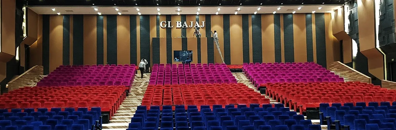 Tiered auditorium seating in red, magenta and blue facing a dark slatted stage wall